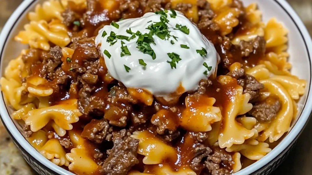 A close-up of a bowl of bowtie pasta topped with a savory ground beef mixture and a dollop of sour cream.